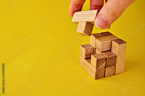 Hand puts the last element of the logical puzzle game wooden cube on a yellow background with a copy space. High quality photo