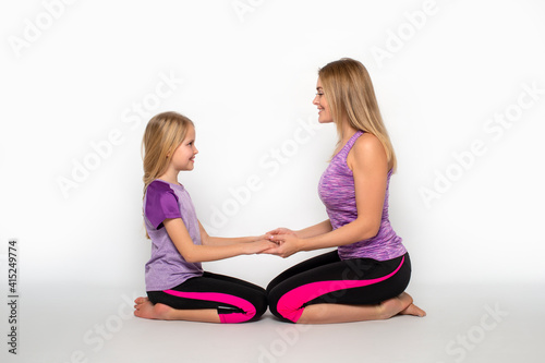 Mom and daughter sit on the floor holding each other's hands with love against white background in studio