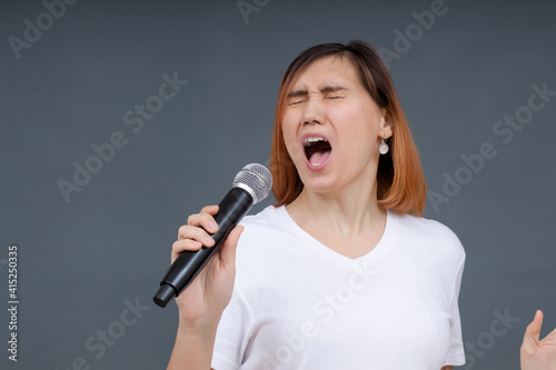 Young beautiful woman singing a song into a microphone while standing on a gray background