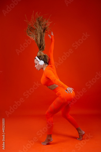 beautiful adult woman in a tracksuit on a red background in headphones 