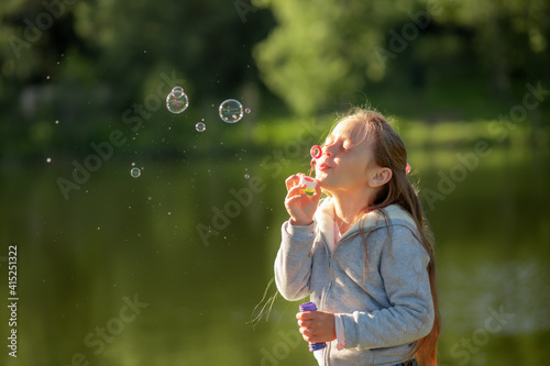 Beautiful little blonde girl  has happy fun cheerful smiling face  soap bubble blower.