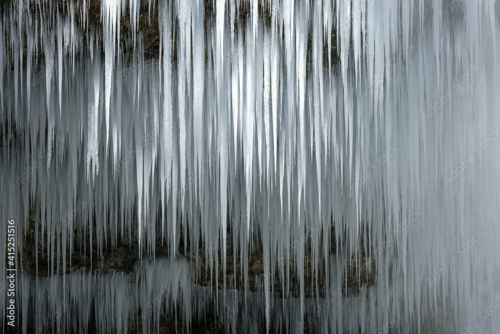 Beautiful long icicles of a frozen waterfall, with water flowing and crashing down and Ice water dripping from the tips of icicles in a cold eery and moody atmosphere in a cave in the mountains 