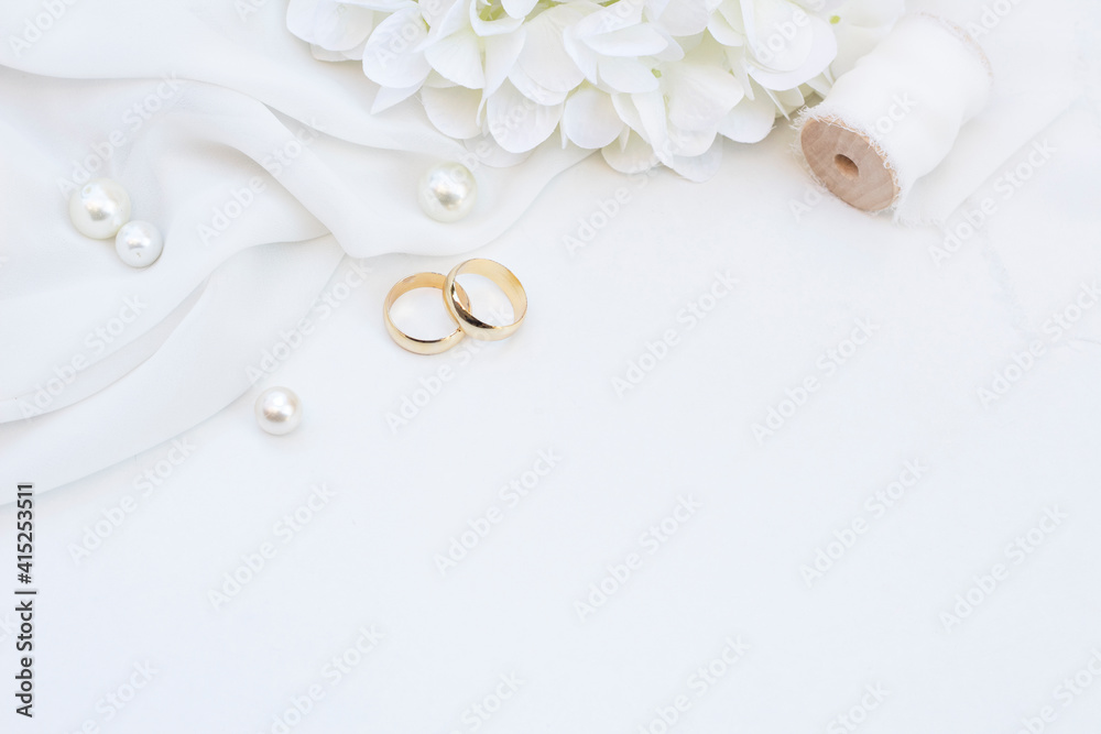 Two gold wedding rings with pearls , flower and ribbon on soft white