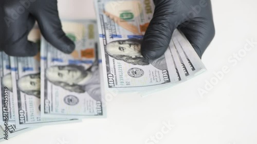 Hands in black gloves are counting money. One hundred US dollar bills.
