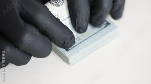 Hands in black gloves are counting money. One hundred US dollar bills.