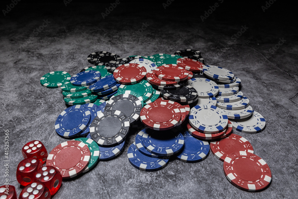 poker chips of different colors scattered on the table next to some red dice with white numbers in the lower left corner on a dark background poker chips of different colors scattered on the table next to some red dice with white numbers in the lower left corner on a dark background