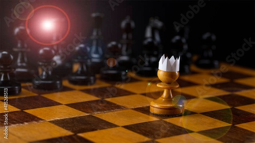 Little brave pawn wearing artificial paper crown suit on chessboard with figures  business entrepreneur leadership concept