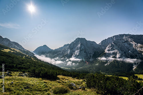 Scenic panoramic view of idyllic rolling hills landscape with blooming meadows and alpine mountain peaks in the background on a beautiful sunny day with blue sky and clouds in summertime © Markus