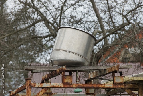 one gray metal barrel lies on the structure for the shower in the yard outside