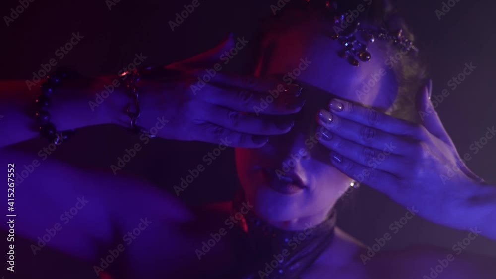 Portrait of a plastic woman dancing an oriental dance in a smoky studio, she is dressed in a revealing costume and illuminated by light. Doing the hand movement. Portrait of a plastic woman dancing an oriental dance in a smoky studio, she is dressed in a revealing costume and illuminated by light. Doing the hand movement.