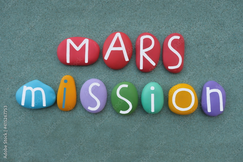Mars Mission logo composed with multi colored stone letters over green sand Mars Mission logo composed with multi colored stone letters over green sand