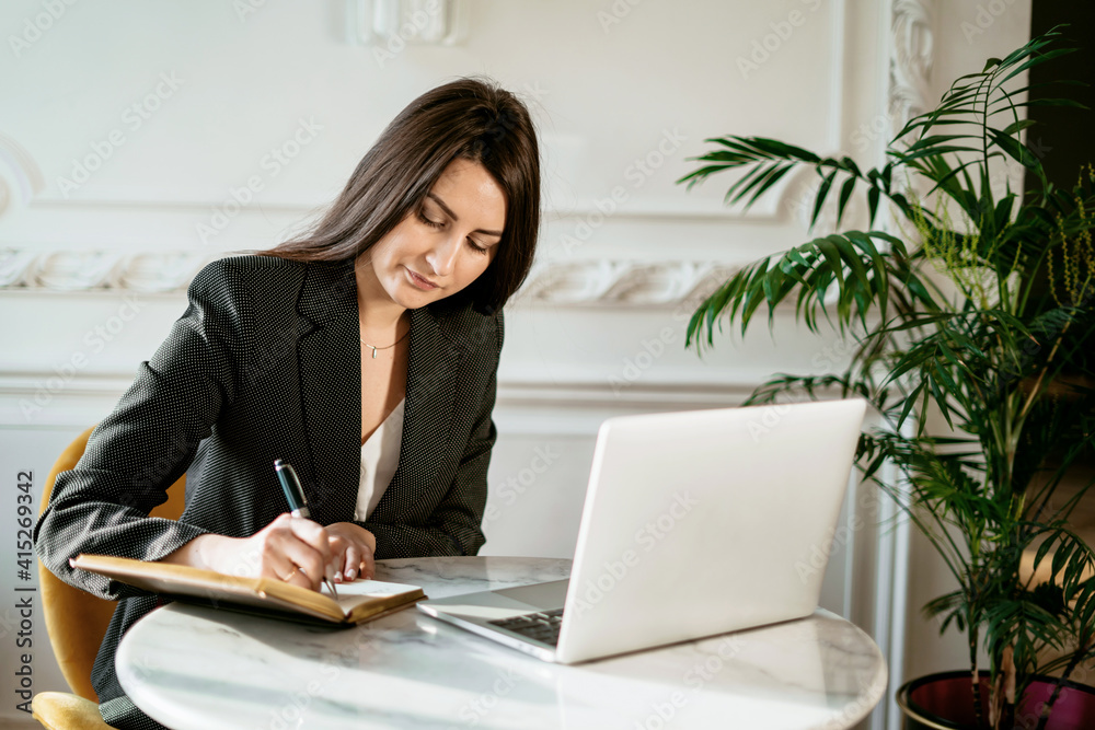 The manager is sitting on the couch working on a laptop computer. A female student in a business suit types a message to colleagues. Modern and stylish office. Calm mood.