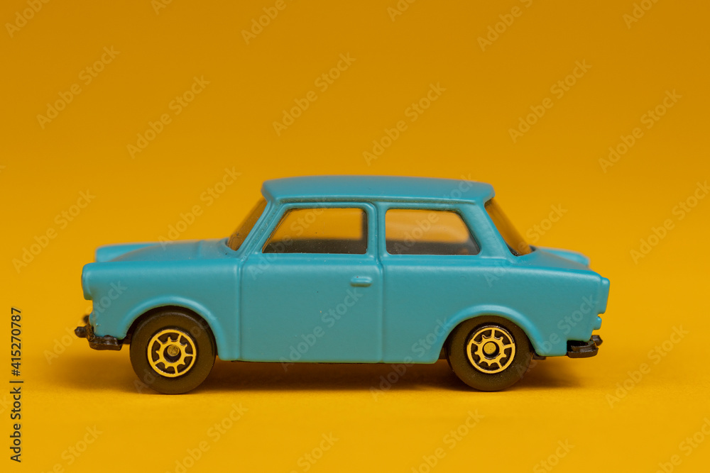 Teal colored miniature car isolated with sharp shadow underneath. Studio still life old fashion toy against a seamless yellow background.