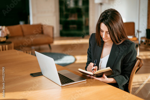 Accountant Manager Student beautiful brunette. A woman writes down important things. New project at work. The lawyer is sitting next to the laptop. Copy space. Works in a modern office.