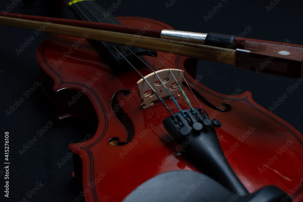 Fototapeta premium Close view of a classical small violin, strings and bridge over a dark black blanket background