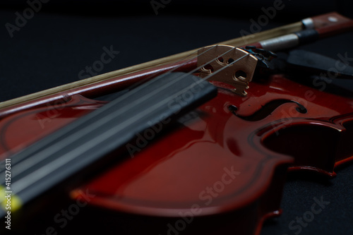 Close view of a classical small violin, strings and bridge over a dark black blanket background 