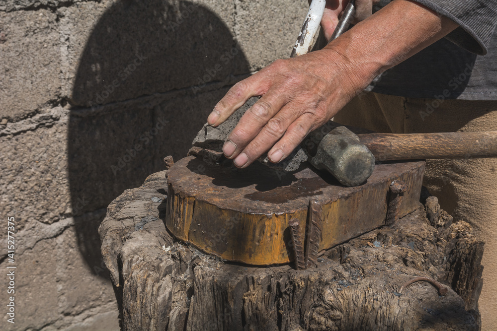 Blacksmith working in the forge with incandescent metal to create chisels by striking the metal into the tool. 
