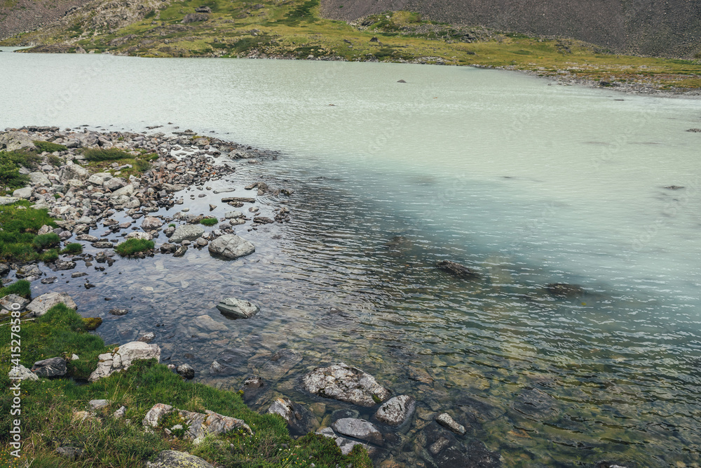 View from top to turquoise mountain lake with transparent water. Atmospheric mountain landscape with turquoise water surface of glacier lake among stones and grass. View from above to highland lake.