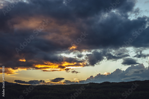 Beautiful mountain scenery with warm golden dawn light in cloudy sky. Scenic contrasting landscape with illuminating color in warm sunset sky. Gold illuminating sunlight. Contrast of warm sunrise sky.