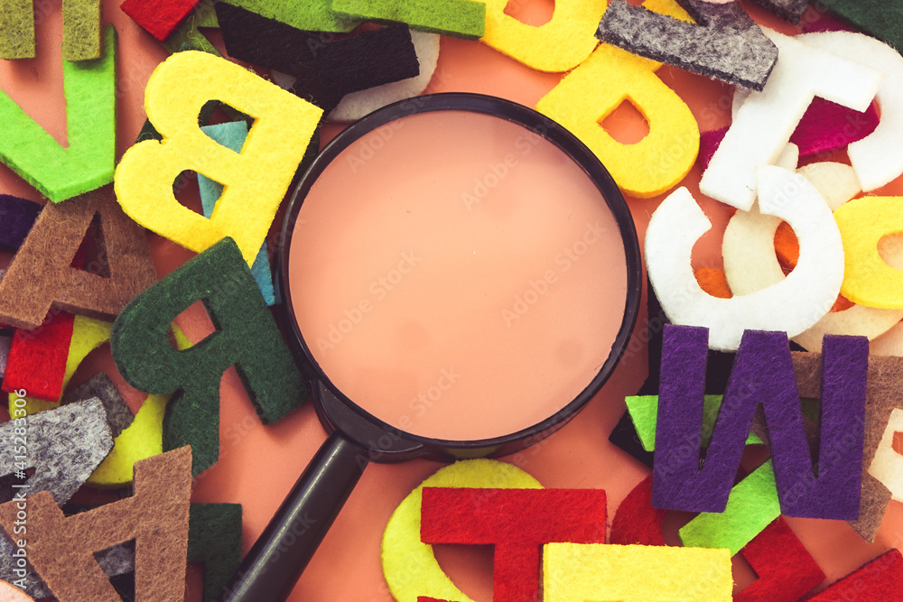 Fototapeta premium Magnifying glass with colorful alphabet on pink background. Education concept.