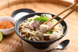 Hand holding chopsticks and eating rice noodle soup with pork, pork ball and vegetables in a bowl, Thai noodles soup