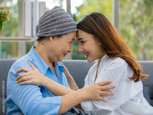 Older Asian woman patient covered the head with clothes effect from chemo treatment in cancer cure process touch her daughter's forehead with happy