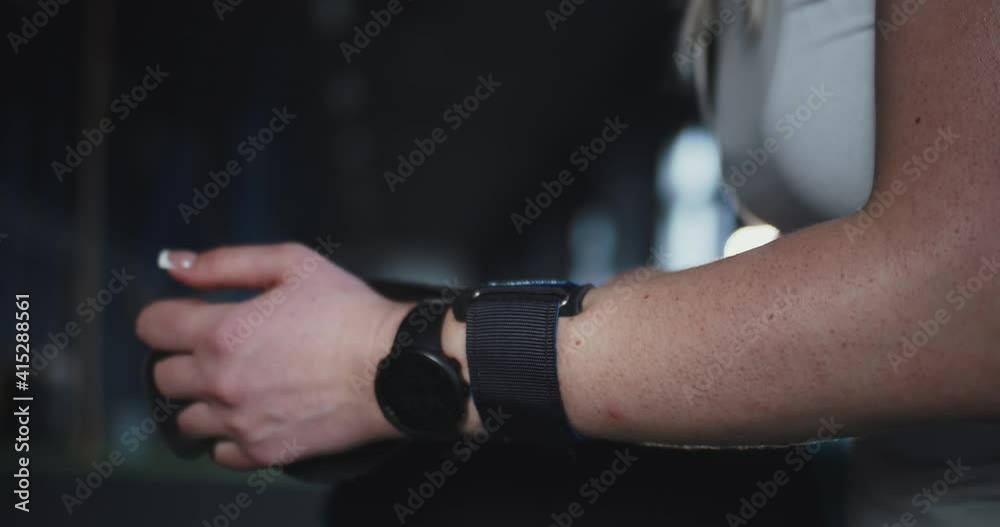 Close-up female cross fit athlete with smart watch puts protective wrist straps on hands preparing to exercise at gym. Close-up female cross fit athlete with smart watch puts protective wrist straps on hands preparing to exercise at gym.