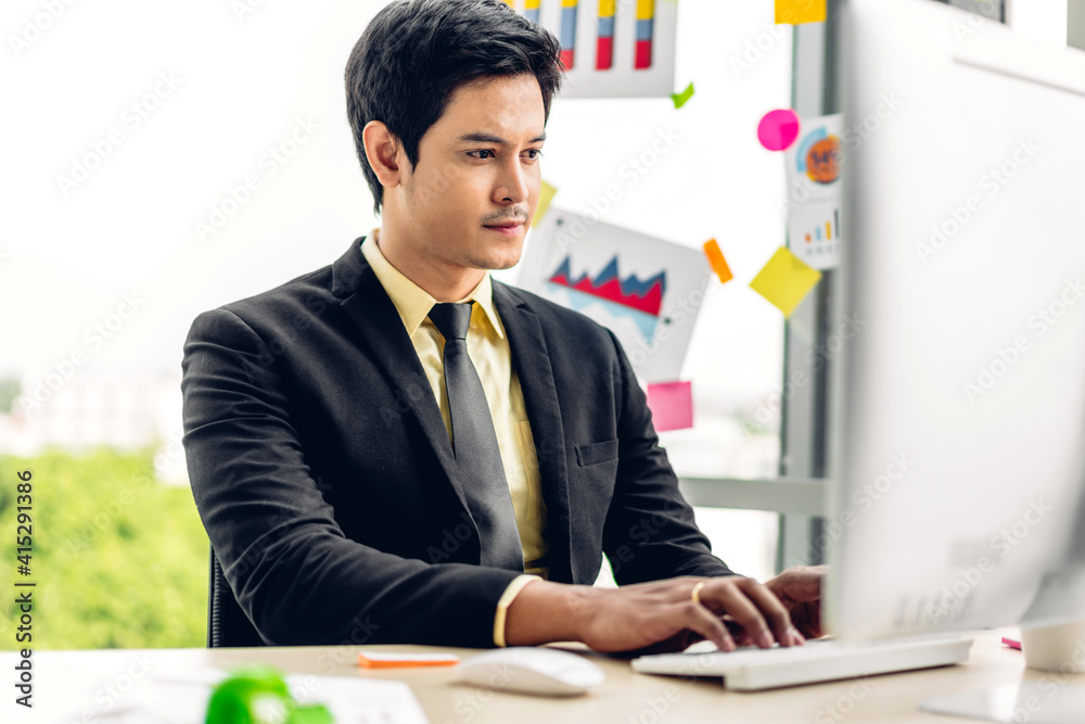 Handsome asian businessman relaxing use technology of desktop computer while sitting on chair.Young creative coworkers business people working and typing on keyboard at office Handsome asian businessman relaxing use technology of desktop computer while sitting on chair.Young creative coworkers business people working and typing on keyboard at office