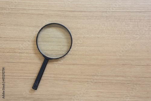 Magnifying glass with black handle on wooden table.