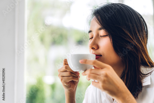 Portrait of smiling happy cheerful beautiful pretty asian woman relaxing drinking and looking at cup of hot coffee or tea.Girl felling enjoy having breakfast in holiday morning vacation on bed at home
