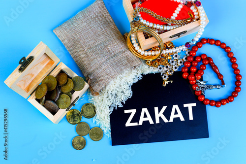 ZAKAT word coin stacked, rice grain in bowl and mini house on brown background. Muslim concept for zakat property, income and "fitrah" zakat.