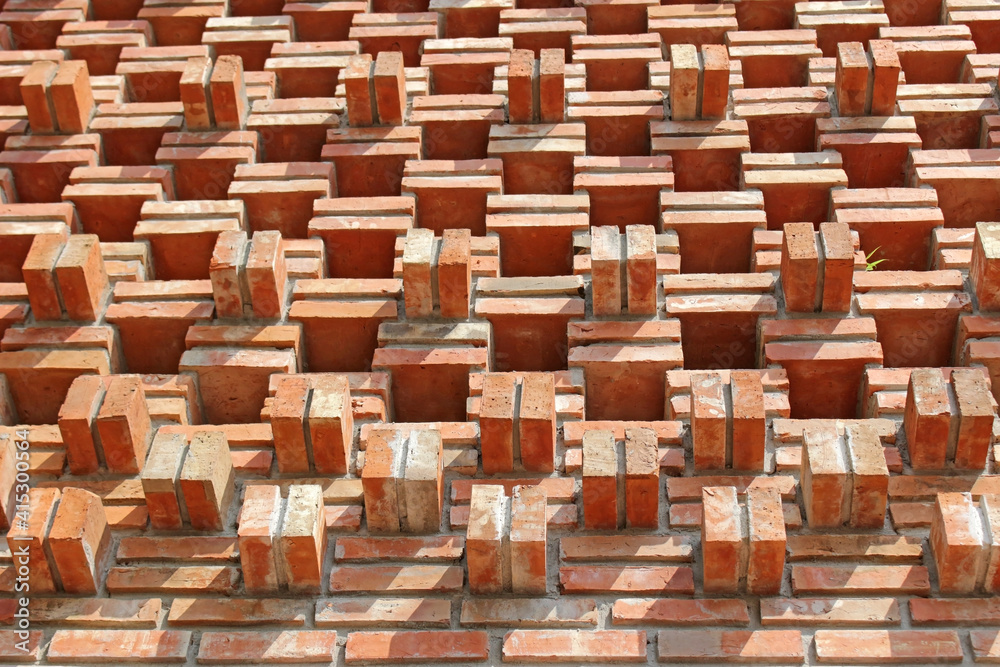 Looking up at an exterior garden wall designed with square holes in the brickwork and bricks that jut out from the wall