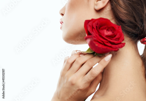 Charming brunette woman holding red flower near her face and cropped view portrait