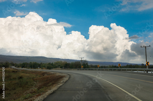An empty road leading to large mountains with large clouds and sky