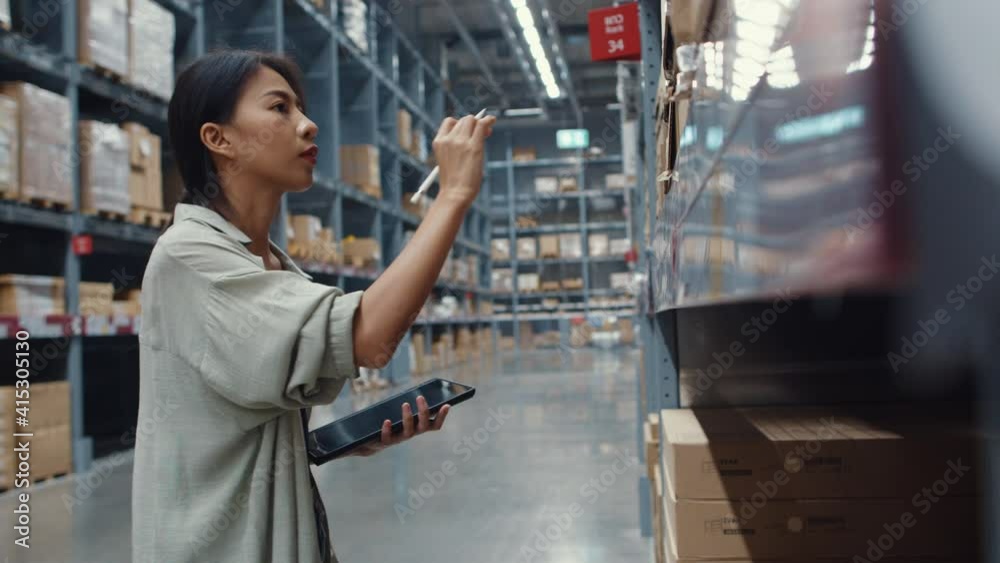Attractive young Asia businesswoman manager looking for goods using digital tablet checking inventory levels standing in retail shopping center. Distribution, Logistics, Packages ready for shipment.