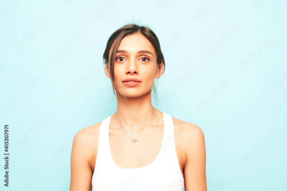 Young beautiful woman looking at camera. Trendy female in casual summer shirt clothes with natural makeup. Funny model posing near blue wall in studio Young beautiful woman looking at camera. Trendy female in casual summer shirt clothes with natural makeup. Funny model posing near blue wall in studio