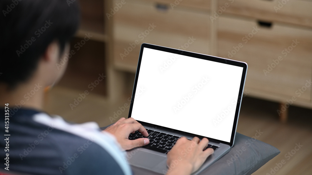 Rear view of casual young man using computer laptop while sitting on couch in living room. Rear view of casual young man using computer laptop while sitting on couch in living room.