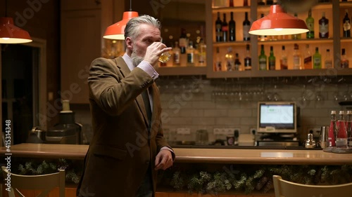Lonely solid gray-haired adult man drinking whiskey alone at the bar in the evening