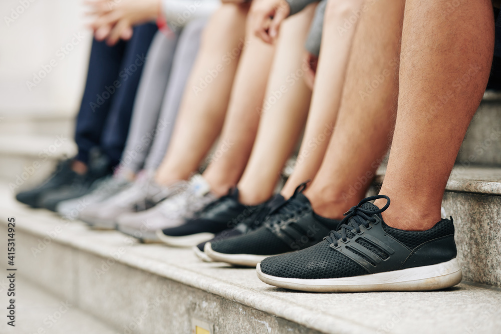 Feet of sportsmen sitting on steps, resting after intense outdoor training, selective focus Feet of sportsmen sitting on steps, resting after intense outdoor training, selective focus