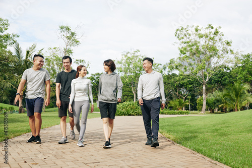 Group of cheerful fit Vietnamese men and women walking in park and discussing outdoor training they just had