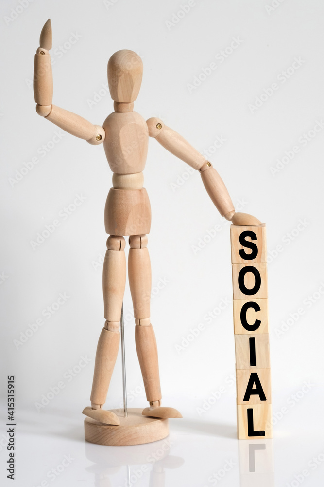 The wooden man raised his hand, and under his left hand he has cubes with the inscription - SOCIAL The wooden man raised his hand, and under his left hand he has cubes with the inscription - SOCIAL