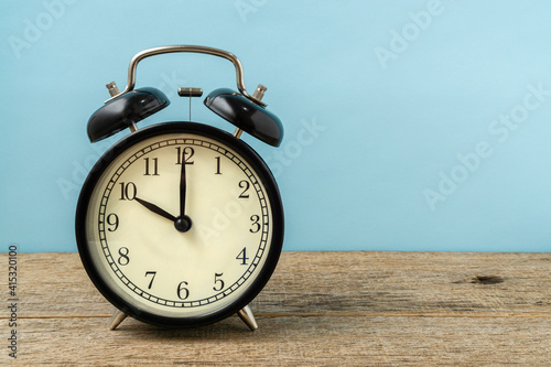 Black vintage alarm clock on a shabby wooden board background shows the time ten hours. Copy space.