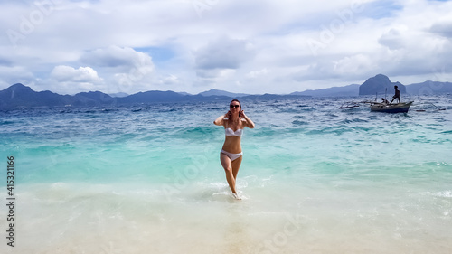 Young traveling woman in white bikini and with sunglasses standing in the ocean. 