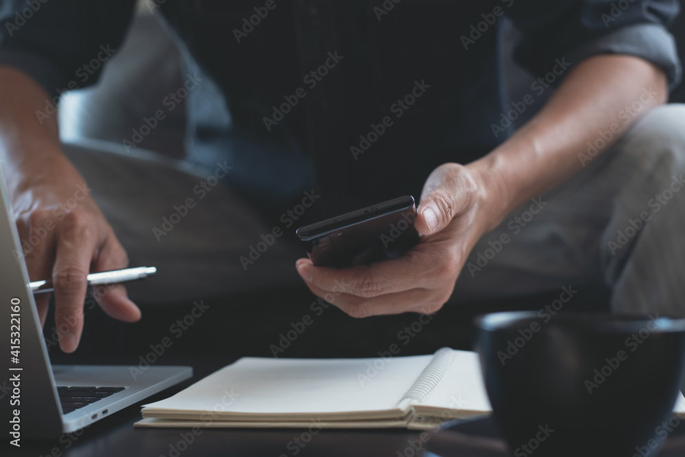 Man using mobile phone during online working on laptop computer on office table Man using mobile phone during online working on laptop computer on office table