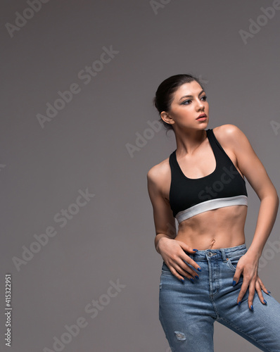 Trendy young woman in a black top in stylish jeans posing on studio. Model pretty beautiful girl posing standing on grey isolated background. Attractive fashionable lady indoors. Copy space