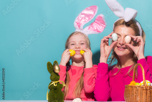 Portrait of mother with daughter wearing rabbit ears with decorating Easter eggs isolated on blue.