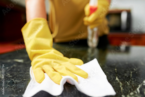 Photography Close-up image of houseiwfe in silicone gloves spraying detergent on kitchen cou