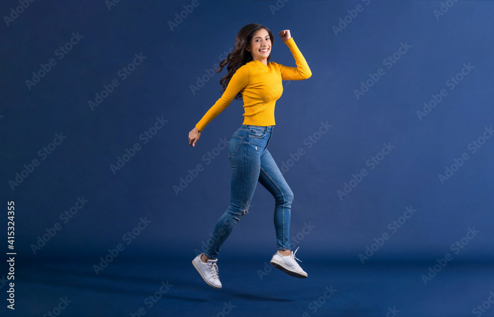 Happy young Asian woman in colorful yellow color casual clothes jumping and running on blue color background, lifestyle and leisure, travel and tourist, travel and vacation,happiness and funny concept