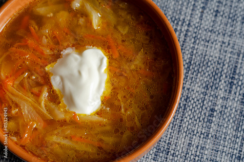Cabbage soup with sour cream in a brown earthen bowl on a blue tablecloth.