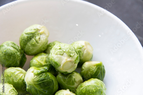 Brussels sprouts in a white bowl on a wood background. Top view, small cabbage, organic food, healthy food. Vegan food.